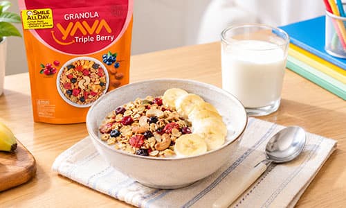 Semangkuk Granola YAVA dengan susu dan irisan pisang untuk sarapan anak usia sekolah.